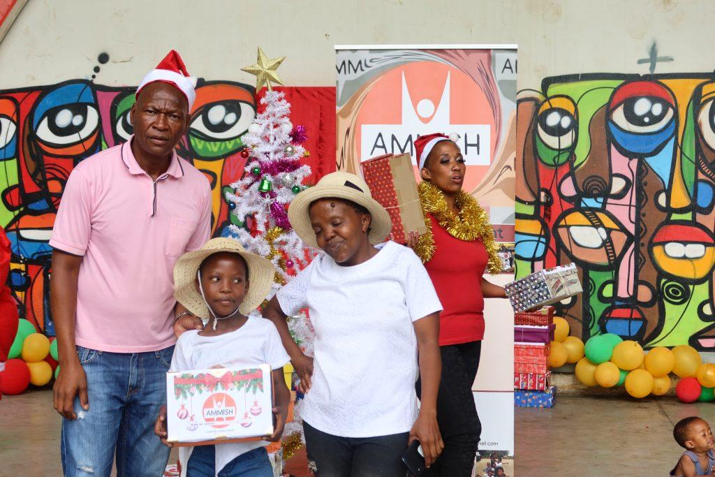 Two children and a man are standing in front of a graffiti wall one child holding a shoebox with presents.