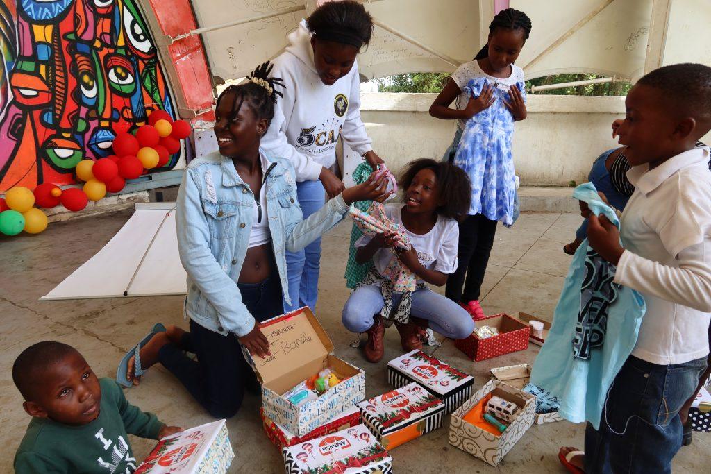 children sitting on the ground holding shoeboxes with presents